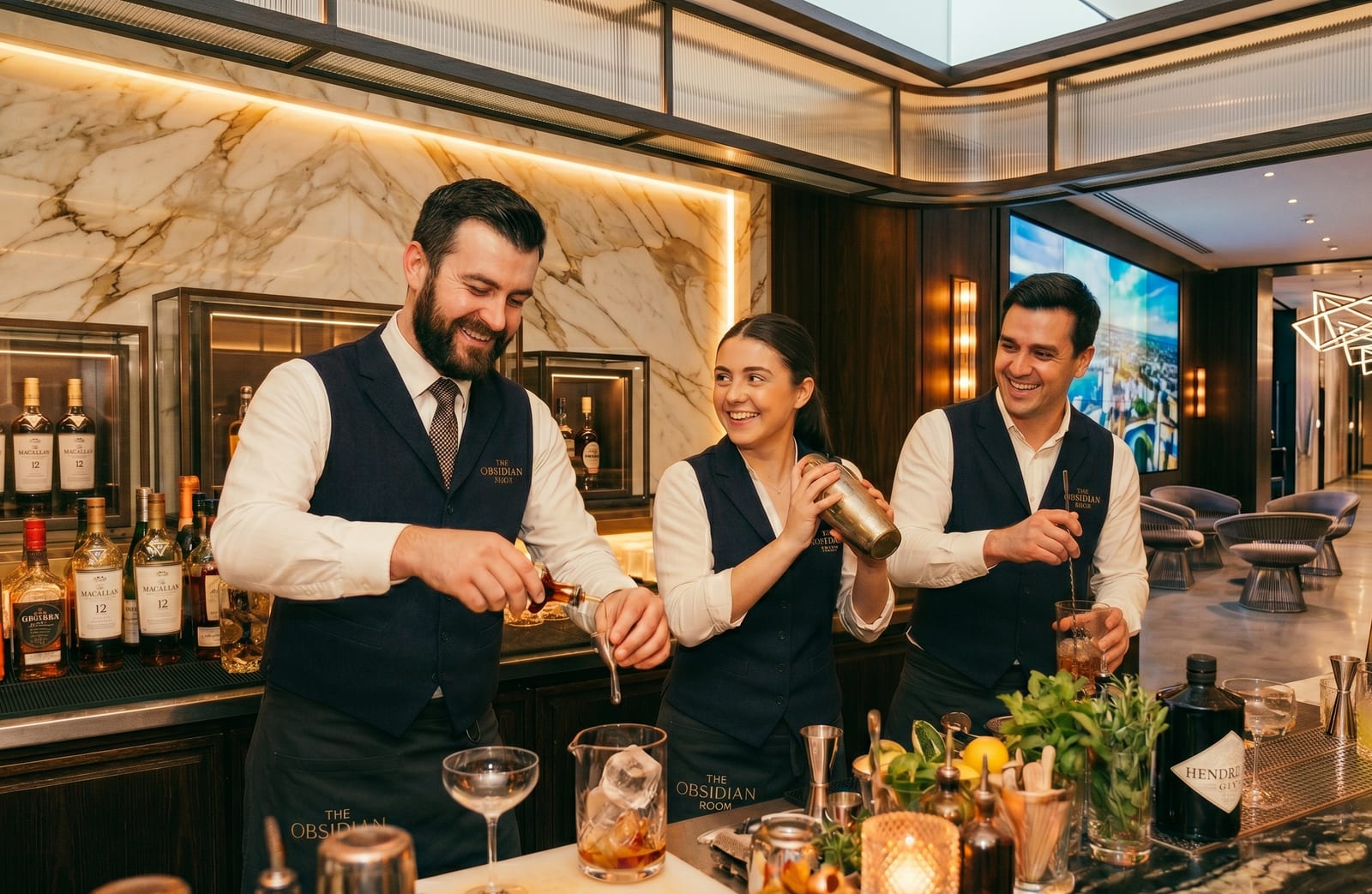 Three bartenders mixing drinks together behind a hotel bar